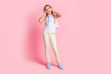 Full size photo of optimistic girl listen music wear white t-shirt sweater trousers sneakers isolated on pink color background
