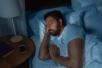 people, bedtime and rest concept - indian man sleeping in bed at home at night