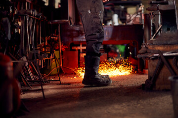 Close Up Of Male Blacksmith Standing Next To Anvil Surrounded By Sparks And Embers