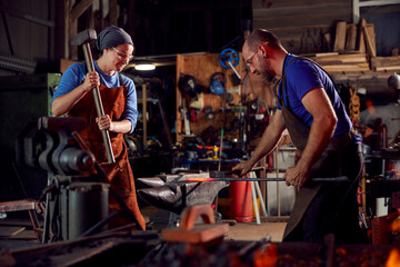 Fototapeta na wymiar Male And Female Blacksmiths Hammering Metalwork On Anvil With Sparks