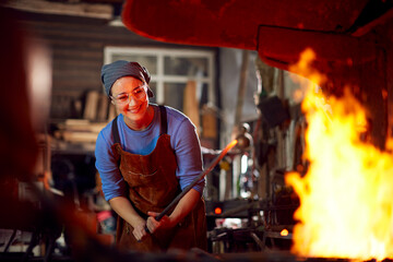 Female Blacksmith Heating Metalwork In Flames Of Forge