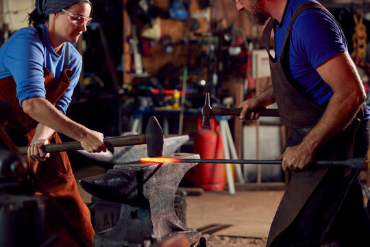 Male And Female Blacksmiths Hammering Metalwork On Anvil With Sparks - Powered by Adobe