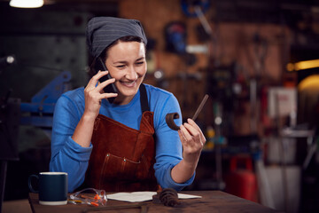 Female Blacksmith Working On Design In Forge Whilst Using Mobile Phone