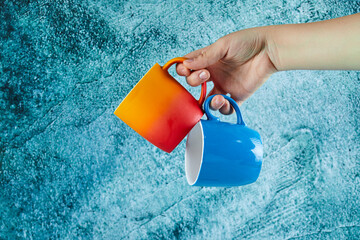Hand holding two mugs on blue background