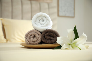 Fototapeta na wymiar Rolled clean towels and flower on bed indoors
