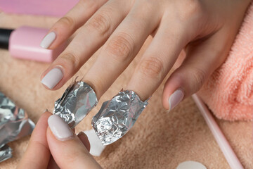 Remove the gel polish with foil. Woman pours remove liquid on a cotton pad, puts it on a nail and...