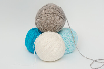 Four balls of yarn for knitting lie in the form of a pyramid on a white background. Gray, white, blue, blue tangle. The concept is needlework. Horizontal photo.