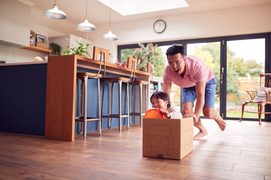 Asian Father And Son Pushing Son Around Kitchen Floor At Home In Junk Modelled Car