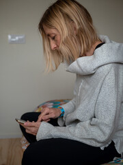 Blonde woman in her bed while talking and writing with her mobile phone