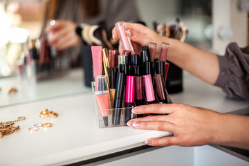 Young woman is neatly organizing her lipstick, lip gloss in the makeup storage at home.