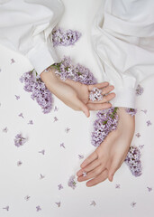 Natural woman cosmetics for hands made of lilac flowers and petals. Moisturize and soften the skin of the hands. Lilac flowers protrude from the sleeves of the arm