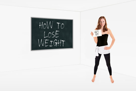 Athletic slim women in front of a chalkboard holding a placard, how to lose weight is written on the board, get fit is written on the paper in her hand