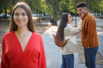 Disloyal man looking at another woman while walking with his girlfriend in park - obrazy, fototapety, plakaty