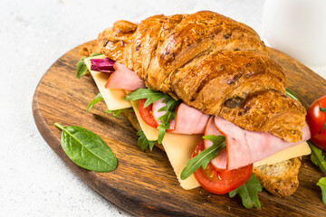 Croissant sandwich with ham, cheese and vegetables on wooden cutting board. Healthy snack or breakfast.