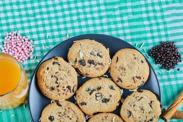 A plate of chocolate chips cookies and a glass of orange juice on dark table with cinnamon