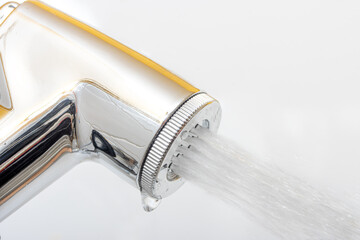 A chrome bidet shower spraying water, close up. The head of the toilet bidet.