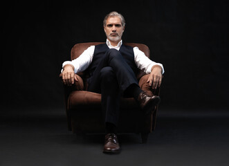 Portrait of handsome elegant mature man with a glass whiskey in a dark room.