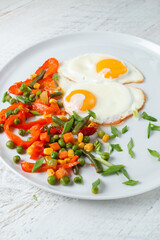 Fried eggs and vegetables in a white plate.