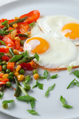 Fried eggs and vegetables in a white plate.