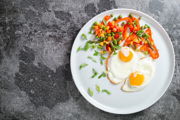 Fried eggs and vegetables in a white plate on a gray concrete stone table for breakfast.