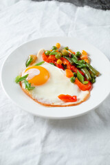 fried eggs and vegetables on a white plate on a table covered with a white tablecloth.
