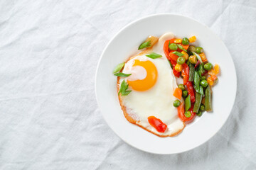 fried eggs and vegetables on a white plate on a table covered with a white tablecloth.