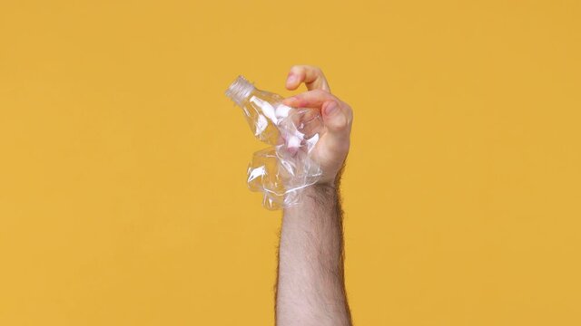 Cropped close up man male hold in hand crush trash empty plastic empty bottle for soda water isolated on yellow background studio Stop nature garbage ecology environment protection concept Save planet
