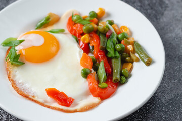 Fried eggs and vegetables in a white plate on a gray concrete stone table for breakfast, close up