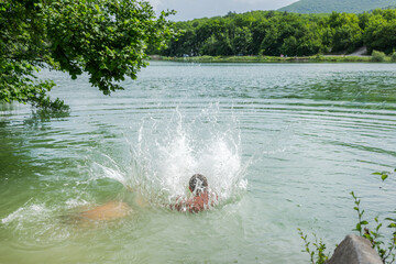 Happy children swim in the lake in the summer. The concept of summer holidays, weekends, holidays. Active lifestyle, outdoor entertainment. A hot summer day. Jump into the water and flying splashes
