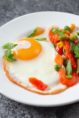 Fried eggs and vegetables in a white plate on a gray concrete stone table for breakfast, close up