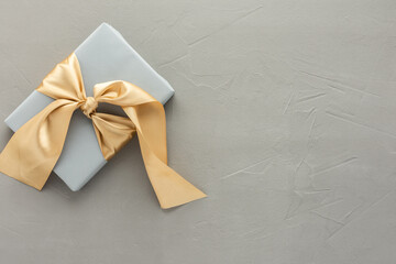 Gray gift box with golden bow on a gray concrete background, birthday or valentine concept, top...