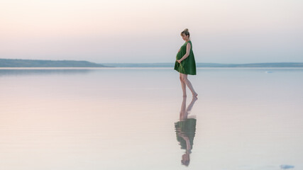Pregnant girl posing at sunset in the water with a reflection