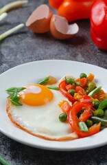 Fried eggs and vegetables in a white plate on a gray concrete stone table for breakfast