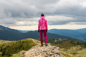 Dramatic landscape with a hiking girl standing on top of a mountain looking into the distance at the beautiful valleys and hills of the Carpathian mountains.