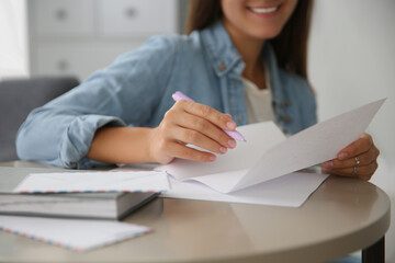 Woman writing letter at table indoors, closeup