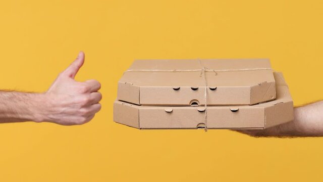 Cropped close up man give male hold in hand pizza cardboard flatbox food order pizza takeaway boxes isolated on yellow background studio. Copy space commercial promo mock up. Delivery service concept