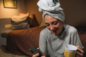 girl applying cosmetic face mask and using mobile phone