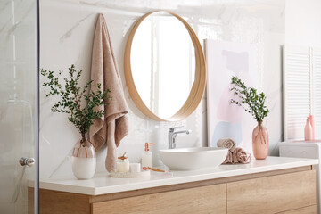 Vase with beautiful branches and toiletries near vessel sink in bathroom. Interior design