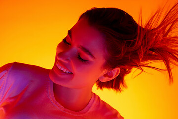 Hair blowing. Caucasian woman's portrait on orange studio background in red-pink neon light. Beautiful female model posing stylish. Concept of human emotions, facial expression, sales, ad, fashion.