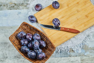 Basket of fresh plums with knife and cutting board on blue table