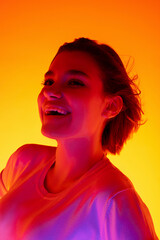 Hair blowing. Caucasian woman's portrait on orange studio background in red-pink neon light. Beautiful female model posing stylish. Concept of human emotions, facial expression, sales, ad, fashion.