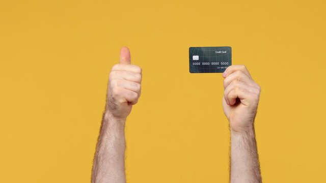 Cropped close up man male hold in hand hold credit bank card showing thumb up like gesture isolated on yellow background studio. Copy space commercial promo advertisement Advertising workspace mock up