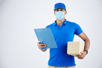 Fototapeta na wymiar Portrait of serious confident young delivery man in medical mask holding document and package