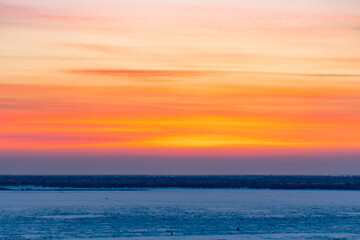 Beautiful sunset over the Amur river in Khabarovsk. Winter. Frozen river. People walk on ice.