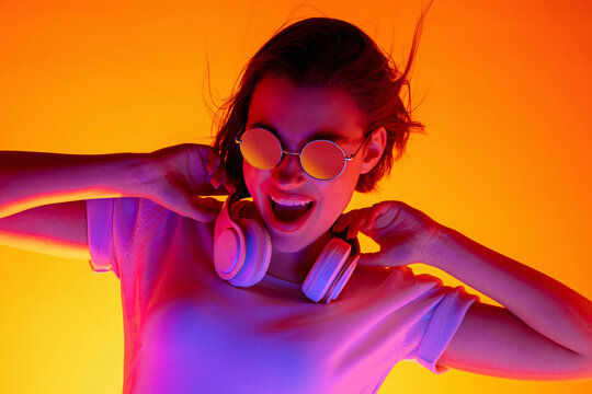 Drive. Caucasian woman's portrait on orange studio background in red-pink neon light. Beautiful female model in sunglasses and device. Concept of human emotions, facial expression, sales, ad, fashion.
