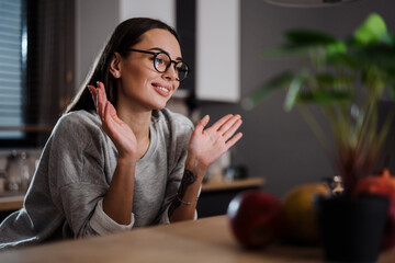 Happy young woman in eyeglasses smiling and gesturing at home