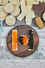 Rice crackers with red and black caviar on a wooden plate