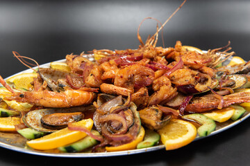 Large pile of spicy shrimp plate served over roasted vegetables and garnished with orange slices.
