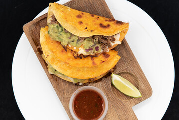 Overhead view of Mexican culinary favorite shrimp quesatacos served on a wooden cutting board and a slice of lime with salsa.
