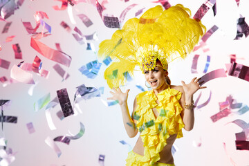 Beautiful young woman in carnival, stylish masquerade costume with feathers dancing on white studio background with shining neoned confetti and bokeh. Concept of celebration, festive time, party